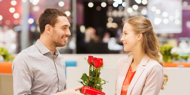 love, romance, valentines day, couple and people concept - happy young man with red flowers giving present to smiling woman at cafe in mall