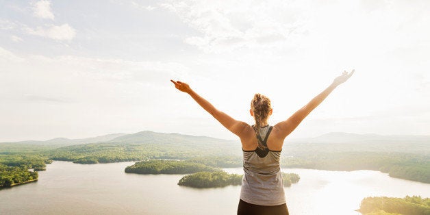  Young woman standing on top of mountain with outstretched arms, rear view