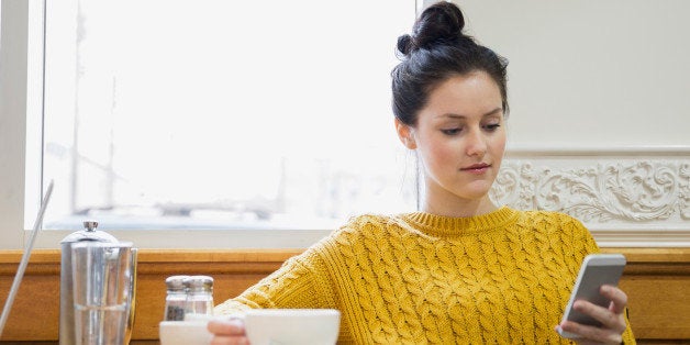 Woman texting and drinking cappuccino in cafe