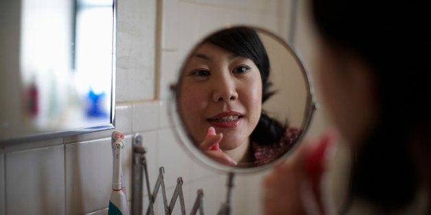 Woman applying lipstick, focus on face in mirror