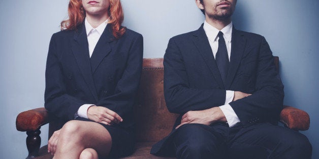 Two sharply dressed business people are waiting on a sofa with a serious expression on their faces. Maybe they're waiting to enter a job interview, or maybe they're a couple waitng to see a divorce lawyer