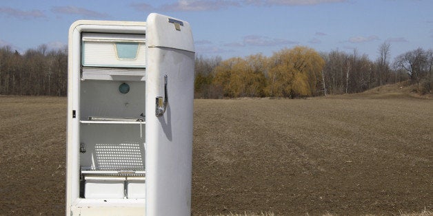 Old open fridge on roadside by farmers field.