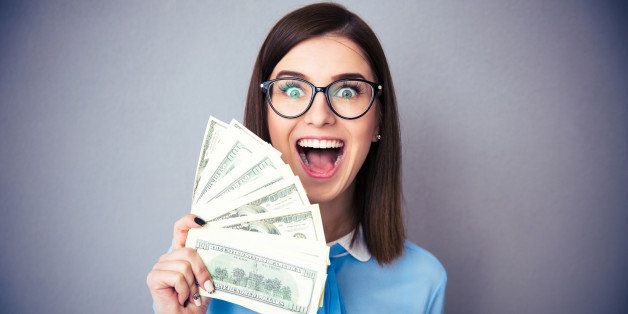 Laughing businesswoman holding bills of dollar and shouting over gray background. Wearing in blue shirt and glasses. Looking at camera