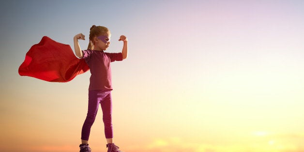 Little child girl plays superhero. Child on the background of sunset sky. Girl power concept