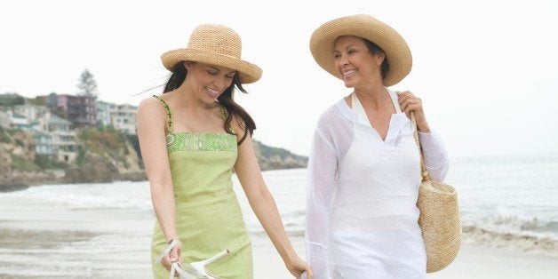 Mother and daughter walk along beach holding hands