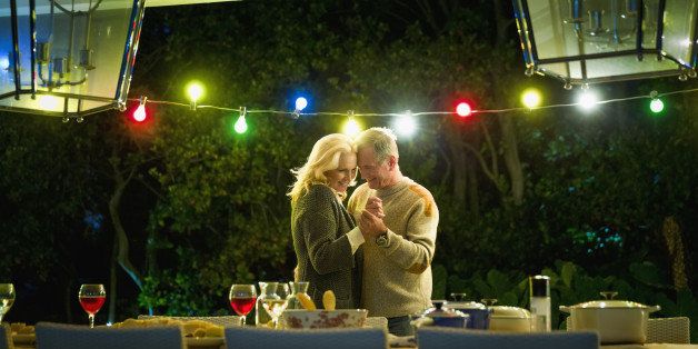 Romantic senior couple dancing at table on illuminated porch