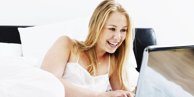 This beautiful young blonde woman lies on her bed obviously enjoying what's on her laptop screen immensely!