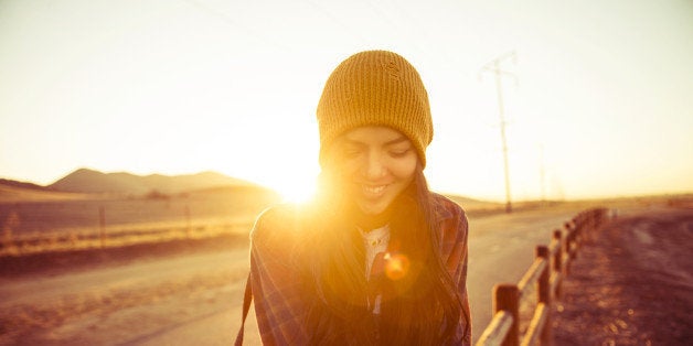 young woman sitting on fence post at sunset