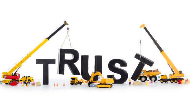 Building up trust concept: Black alphabetic letters forming the word trust being set up by group of construction machines, is