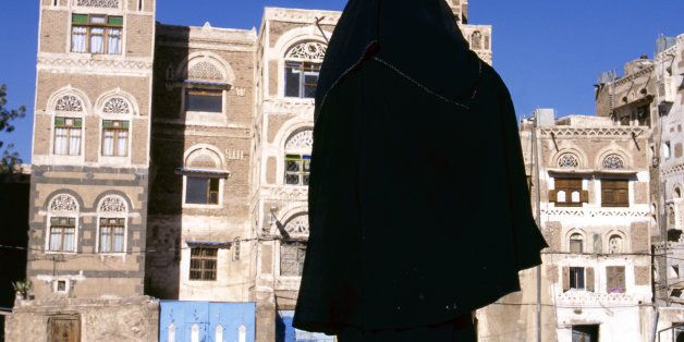A veiled Muslim woman walks on a Sana a street, Yemen.At background typical Yemen houses.