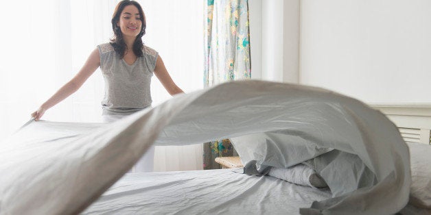 USA, New Jersey, Young woman spreading sheet on bed