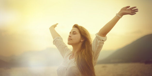 freedom concept, woman with arms raised in sunset field.