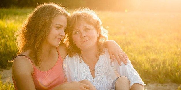 Happy mother sitting on grass in nature with her teenage daughter, flare from setting sun in photo