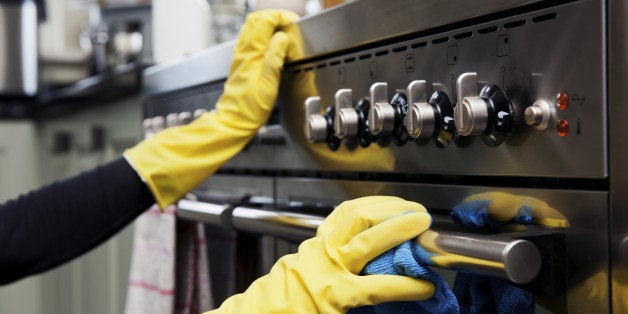Closeup photograph of two hands cleaning the oven in a domestic kitchen.