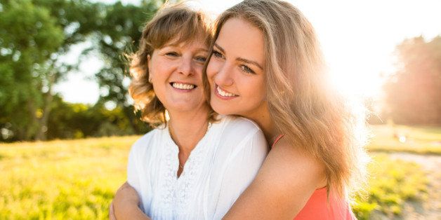 Mother and her teenage daughter hugging outdoor in nature with setting sun in background, wide angle.