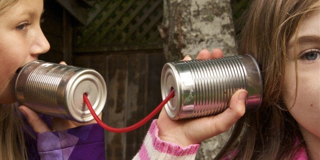 Two girls talking using tin cans connected by red string.