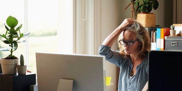 Stressed woman with hand in hair holding credit card at computer in home office