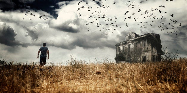 Man walking in a field towards a haunted house