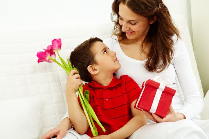 Cute lad with bunch of beautiful tulips looking at his mother with giftbox