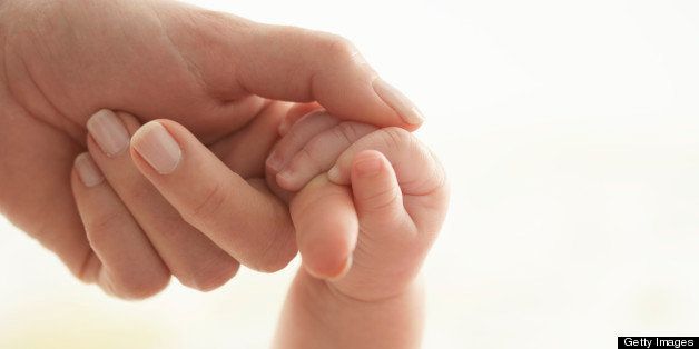 Baby girl (3-6 months) holding woman's hand, close-up