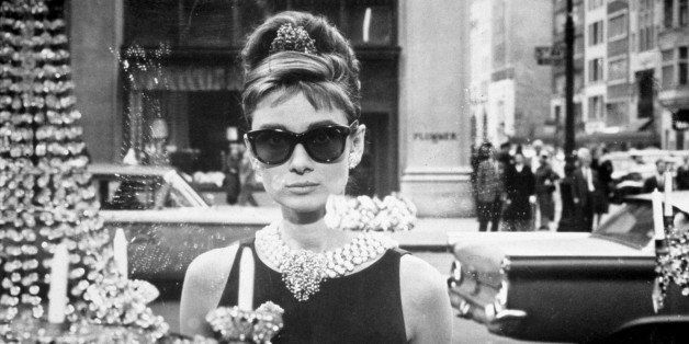 1961: Belgian-born actor Audrey Hepburn (1929 - 1993), as Holly Golightly, holds a cup and a paper bag while looking into one of the window displays at Tiffany's in a still from the film, 'Breakfast at Tiffany's,' directed by Blake Edwards. She wears sunglasses, a little black dress, long gloves and a tiara in her chignon. (Photo by Paramount Pictures/Getty Images)