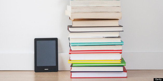 E-reader digital tablet sitting next to a stack of traditional hardcover books on the floor.