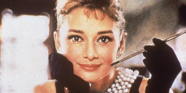 Belgian-born actress Audrey Hepburn (1929 - 1993), in a black, shoulderless dress, matching gloves, and a tiara, smiles with