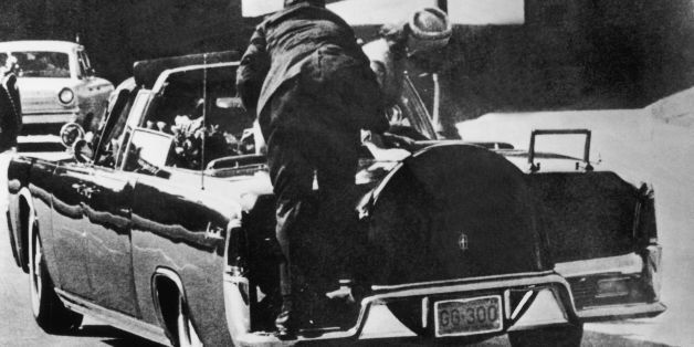 UNITED STATES - NOVEMBER 22: November 22, 1963. Just after John F. KENNEDY, president of the United States, has been hit by bullets, Jacqueline KENNEDY stands up in the presidential car to lift up the body of her husband. In the foreground, the body guard riding on the back fender leans toward them. (Photo by Keystone-France/Gamma-Keystone via Getty Images)