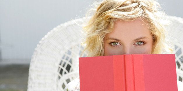 Young woman peeking over open book.