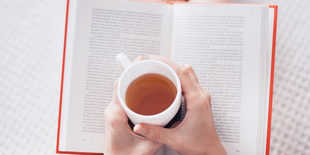 Close-up of female hands holding teacup in front of opened book