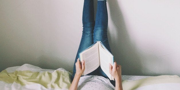 Woman Lying On Bed Reading Book With Legs Raised