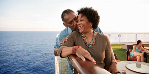 Mature African American man kissing the cheek of African American woman while both lean on rail on deck of a cruise ship