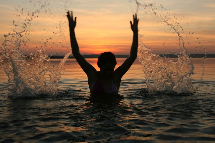 girl very splashing in the water at the beach creating many splashes over their heads against the backdrop of setting sun