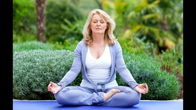 mature woman doing lotus yoga position outside in the garden