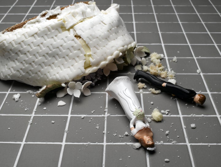 Bride and groom figurines lying at destroyed wedding cake on tiled floor