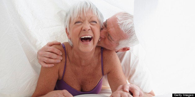 Caucasian couple playing under sheet in bed