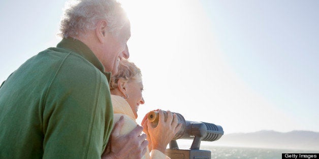 Smiling senior couple looking at ocean with coin-operated binoculars