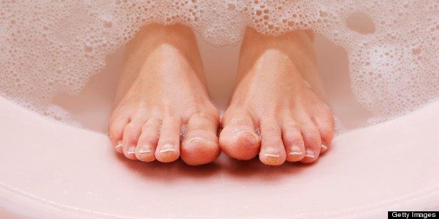 woman's feet resting against bath tub with bubbles