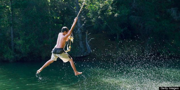 Teenage boy (13-15) swinging on rope over lake, rear view