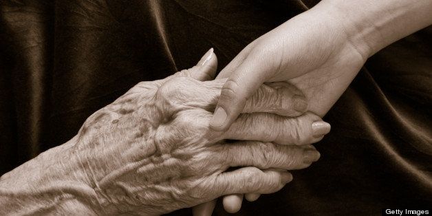 young hand holding old hand with arthritis, reaching and holding on dark cloth background