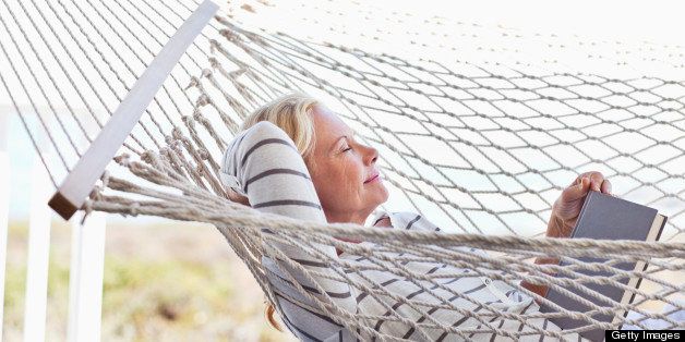 Mature woman relaxing in hammock with a book, eyes closed