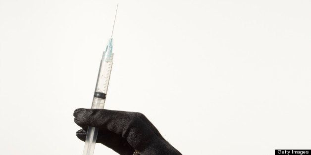 A female hand in a black evening glove holding a hypodermic syringe. 