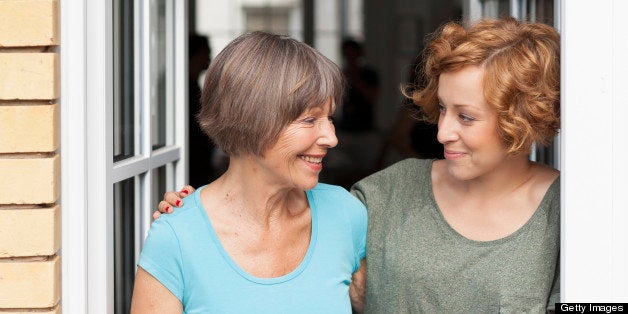 A senior mother with her adult daughter looking at each other, at open window, beautifully illuminated by the warm afternoon