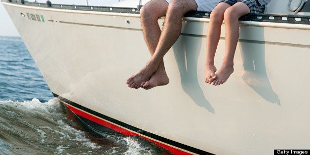 Father and son sitting on yacht, legs dangling