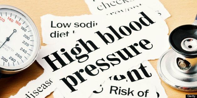 Close up on high blood pressure headline with other related press stories, stethoscope, and blood pressure gauge on wooden desk. 