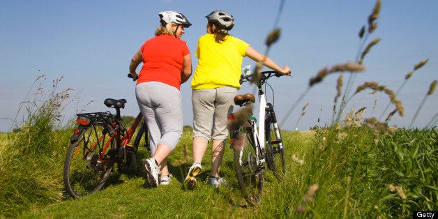 Two friends walking with bicycles through field