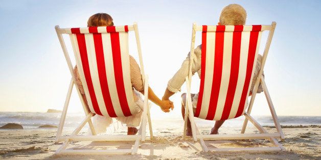 Senior couple relaxing in striped deck chairs on the beach and holding hands