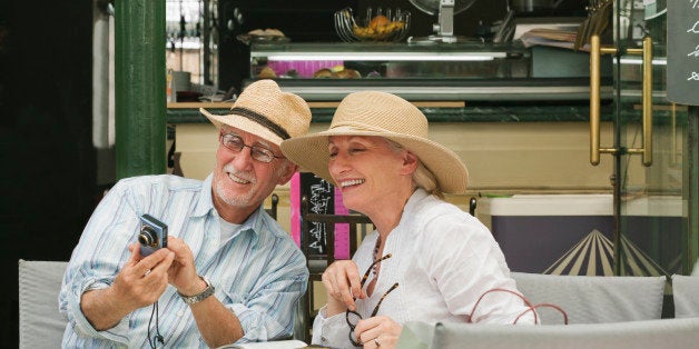 Mature couple seated in sidewalk cafe sharing photos of their trip.