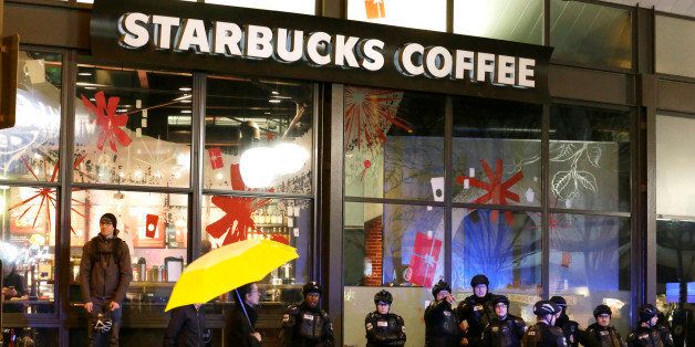 Bicycle police watching over a protest stand next to a Starbucks coffee store as a pedestrian walks by with an umbrella, Monday, Dec. 8, 2014, in downtown Seattle. Police were keeping an eye on a demonstration against the decisions not to indict police officers who who killed men in Ferguson, Missouri and New York. (AP Photo/Ted S. Warren)