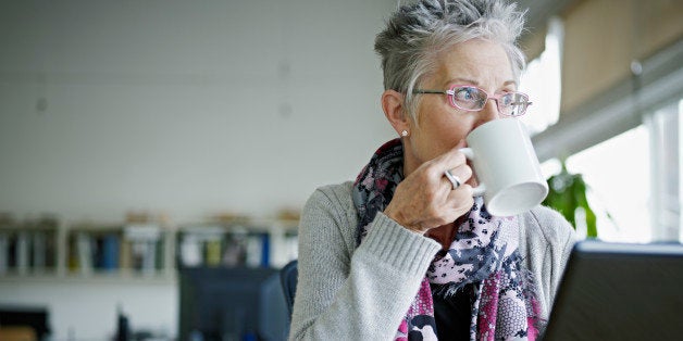 Businesswoman sitting at laptop in office drinking coffee looking out window